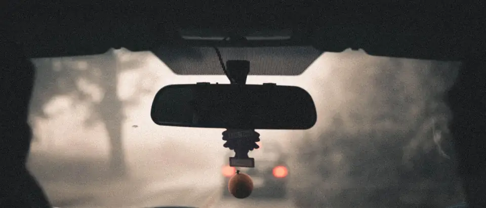 The view through a windshield on a misty road, with the rear-view mirror and the unit behind it