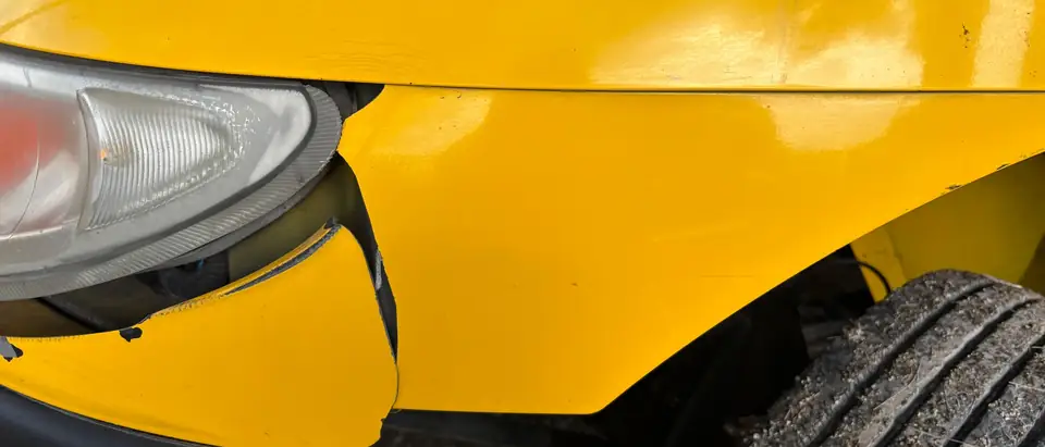 The front corner of a yellow car, its bumper cover cracked by the headlight