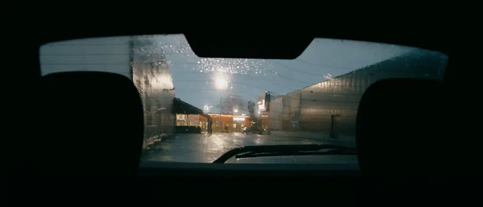 A wet rear window at night seen from inside a car, its defroster lines across the glass