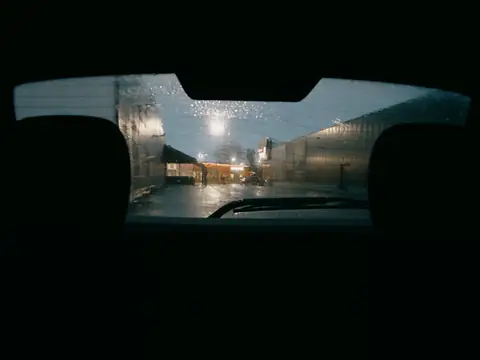 A wet rear window at night seen from inside a car, its defroster lines across the glass