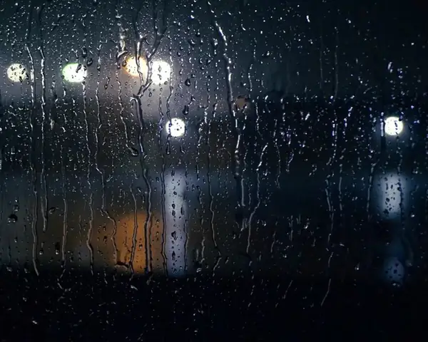 Rain running down glass at night, with white and amber lights out of focus behind it