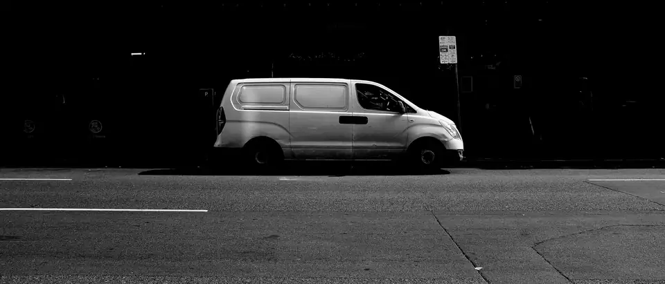 A plain white van parked on a dark street at night