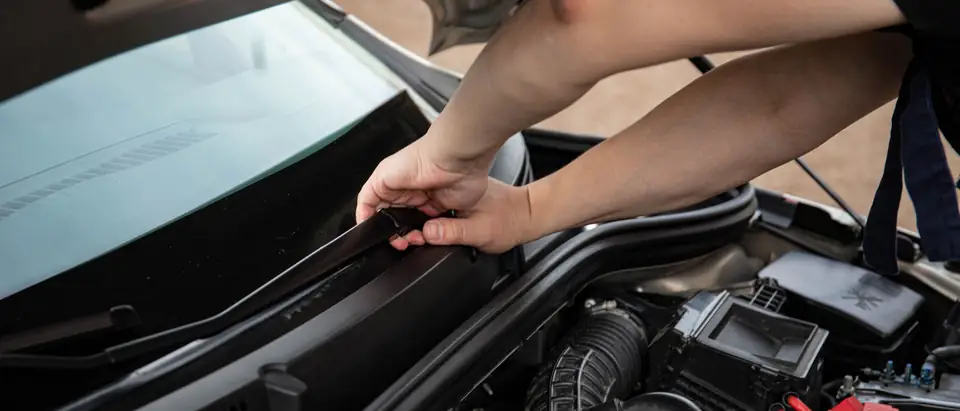 Hands fitting the cowl trim at the base of a windshield, the hood raised